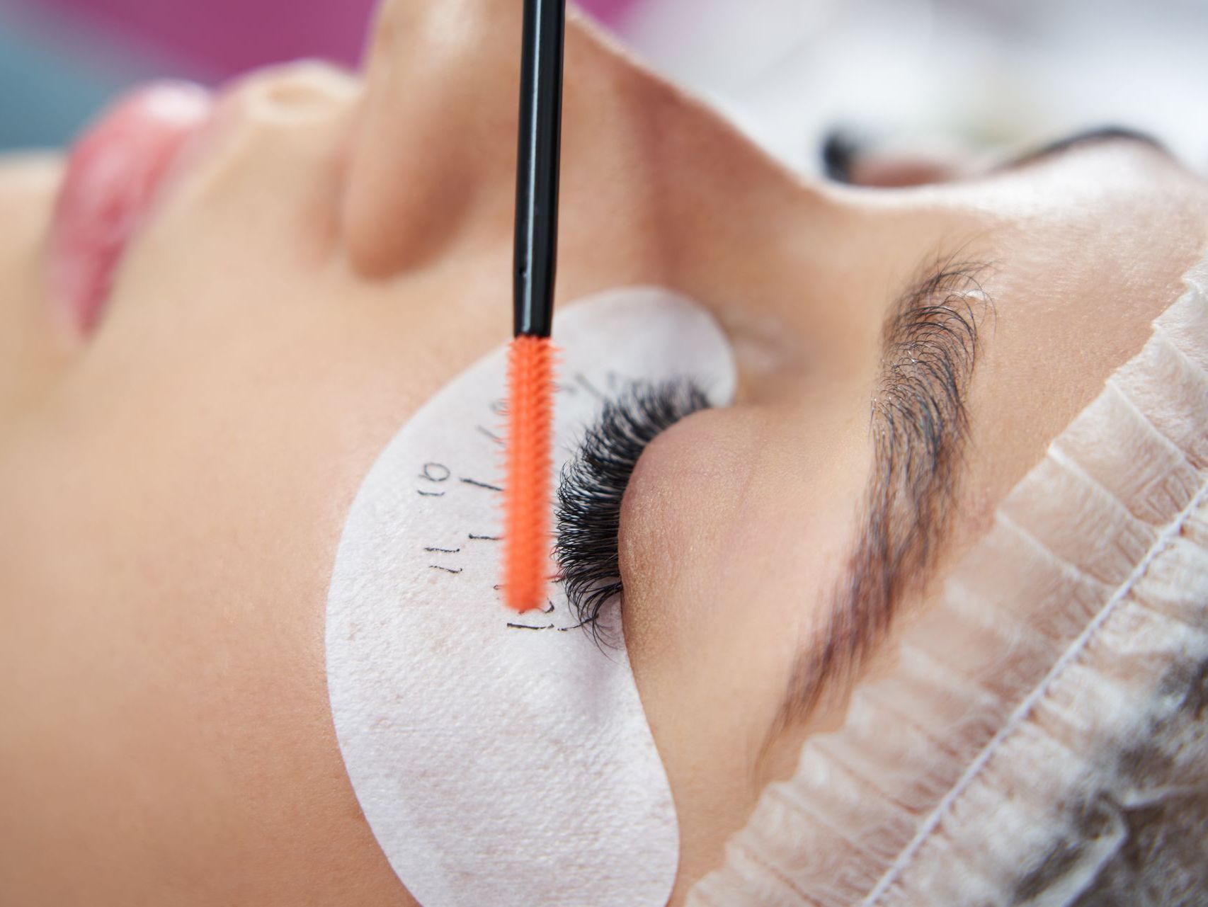 Woman receiving eyelash extensions, applicator over eye with measuring guides.