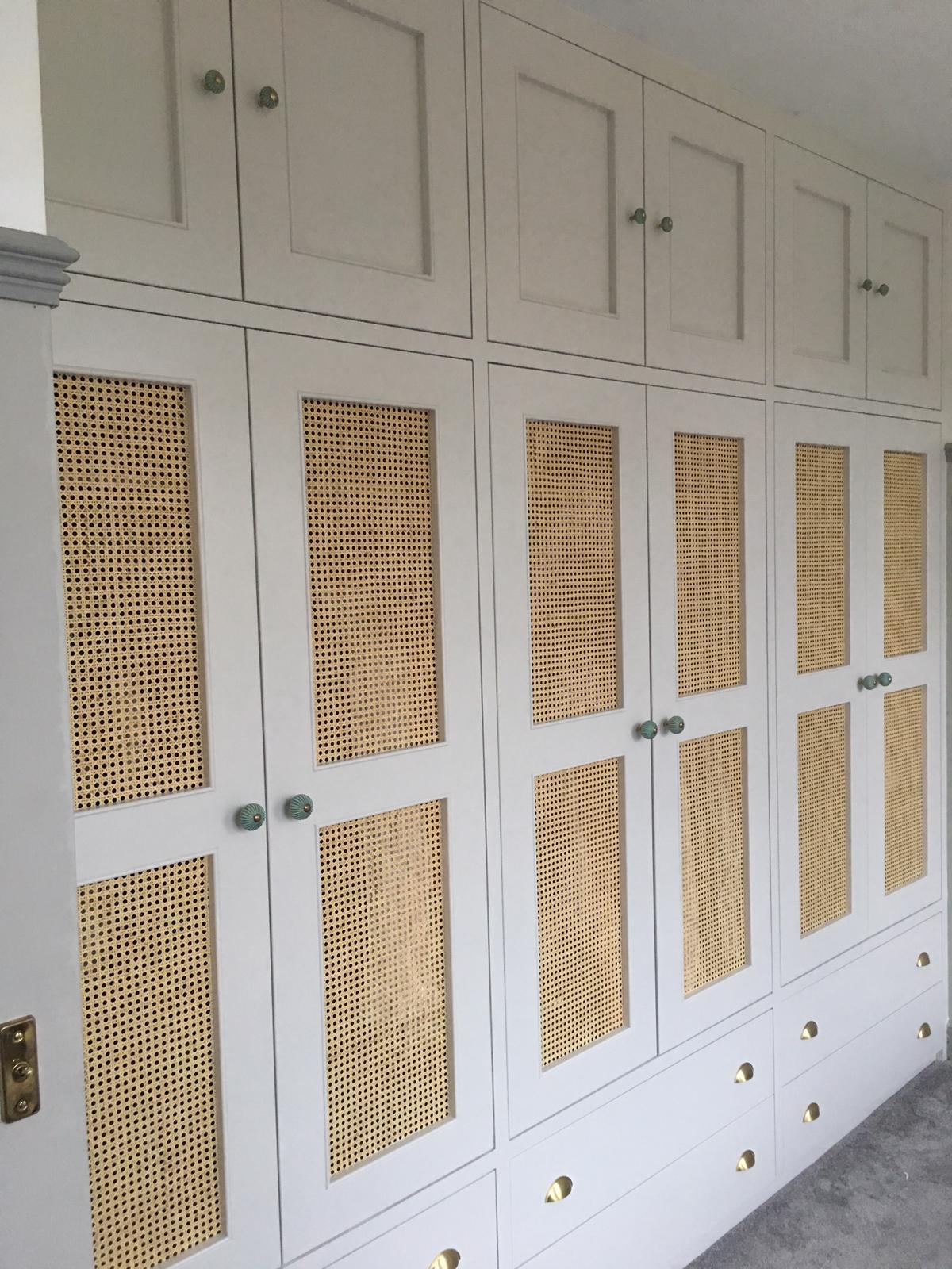 A large white wardrobe with drawers and the bottom , shaker rattan style doors to the middle section, and smaller shaker doors at the top.