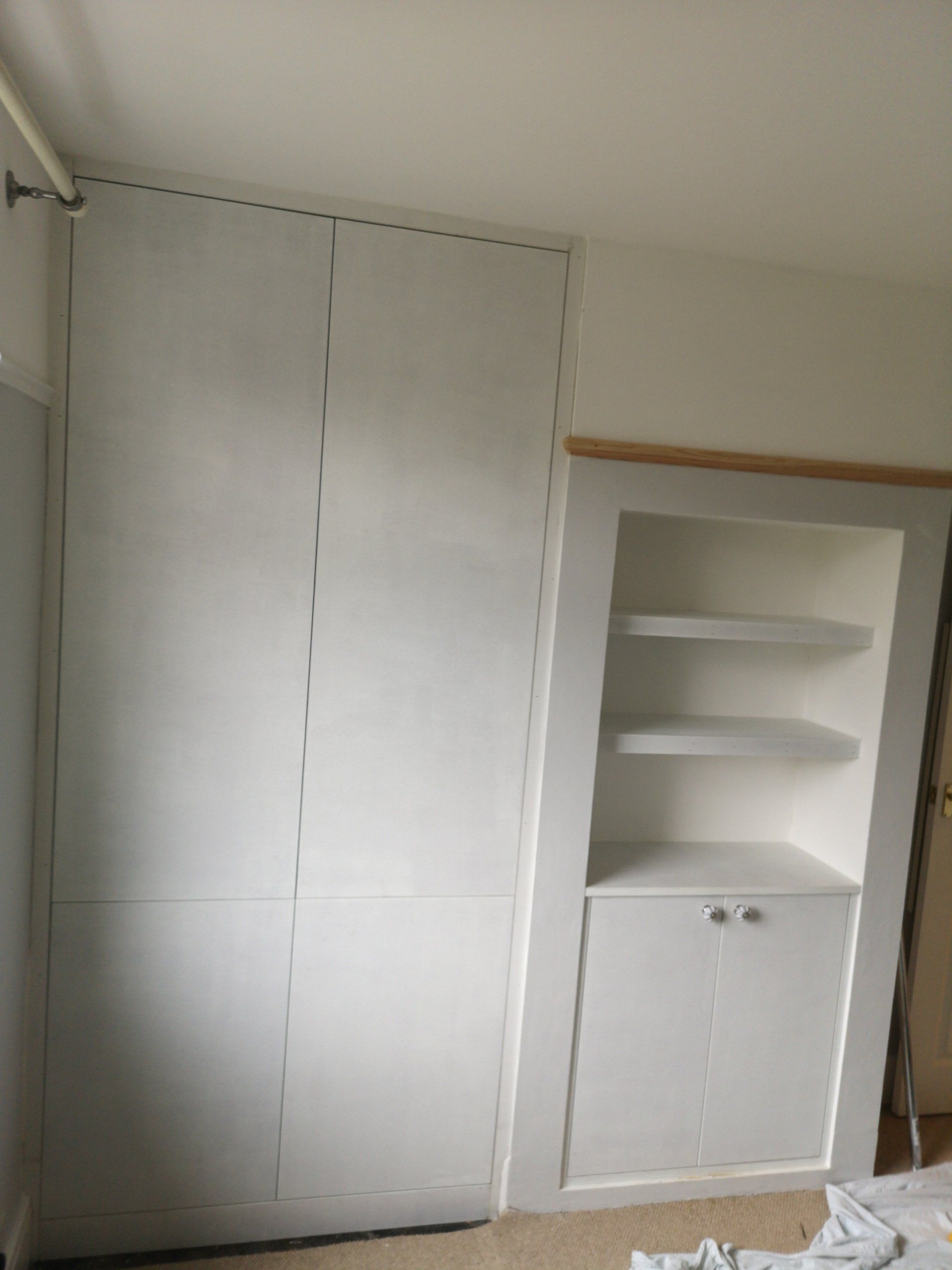 A white fully painted Alcove wardrobe with small cupboard and floating shelves in fire place next to wardrobe.