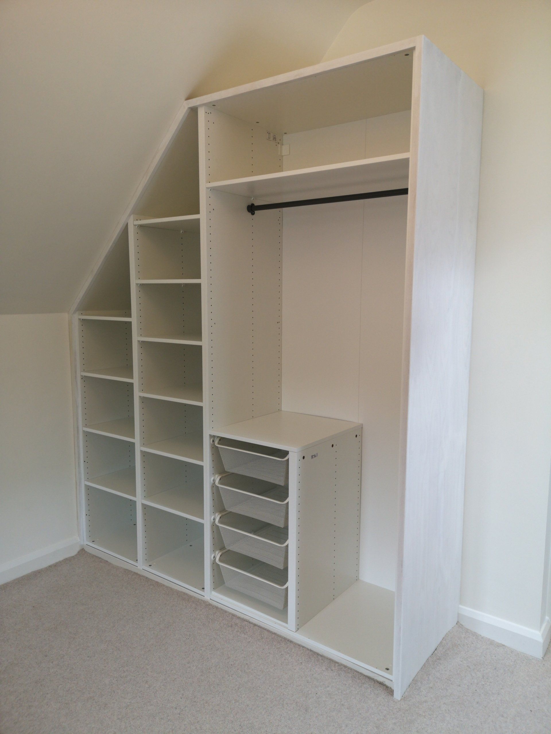 A large white wardrobe with Ikea carcasses cut to fit sloped ceiling in bedroom.
