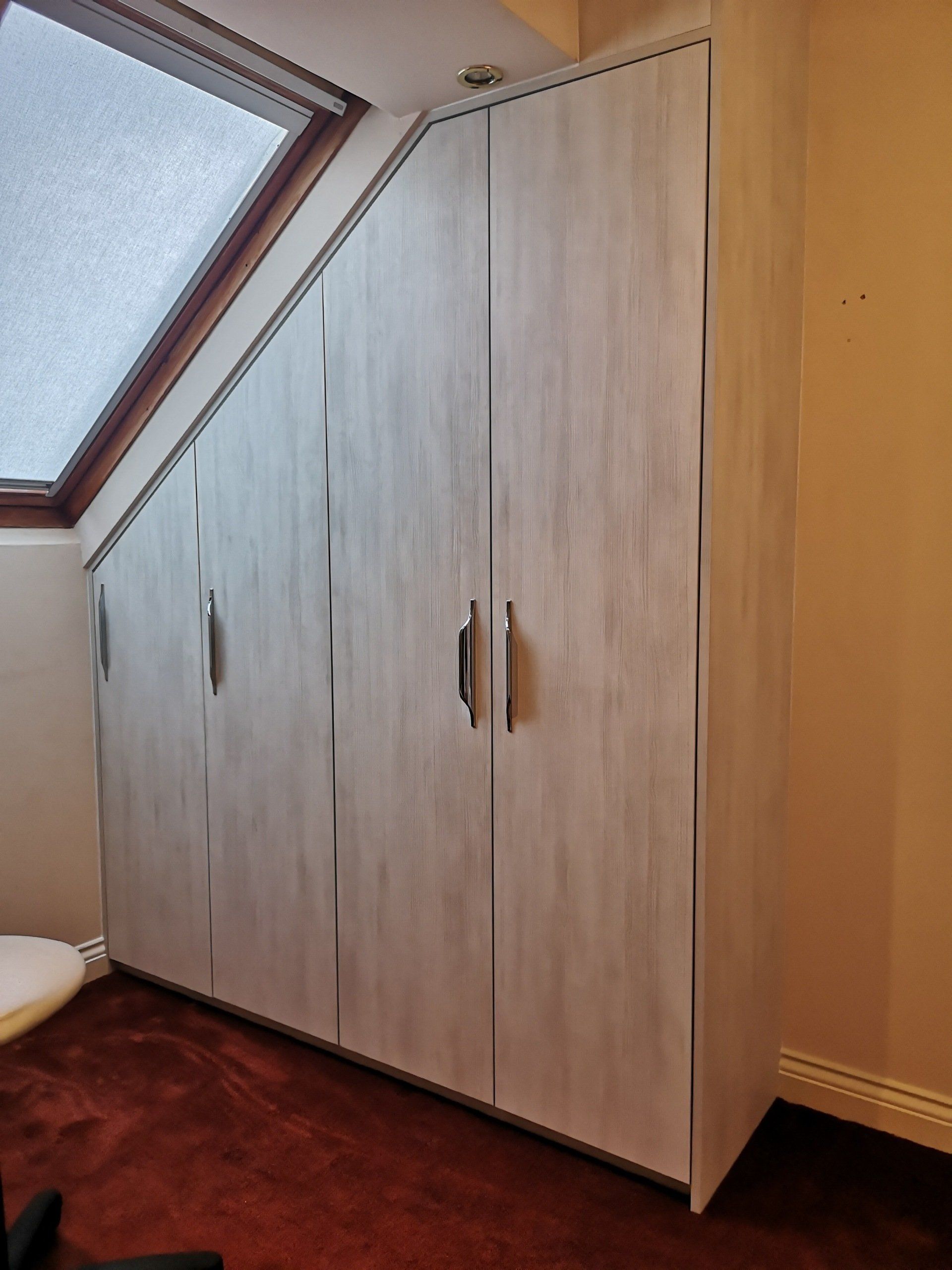 A bespoke pre finished white wood grain wardrobe fitted in a loft conversion with a sloped ceiling.