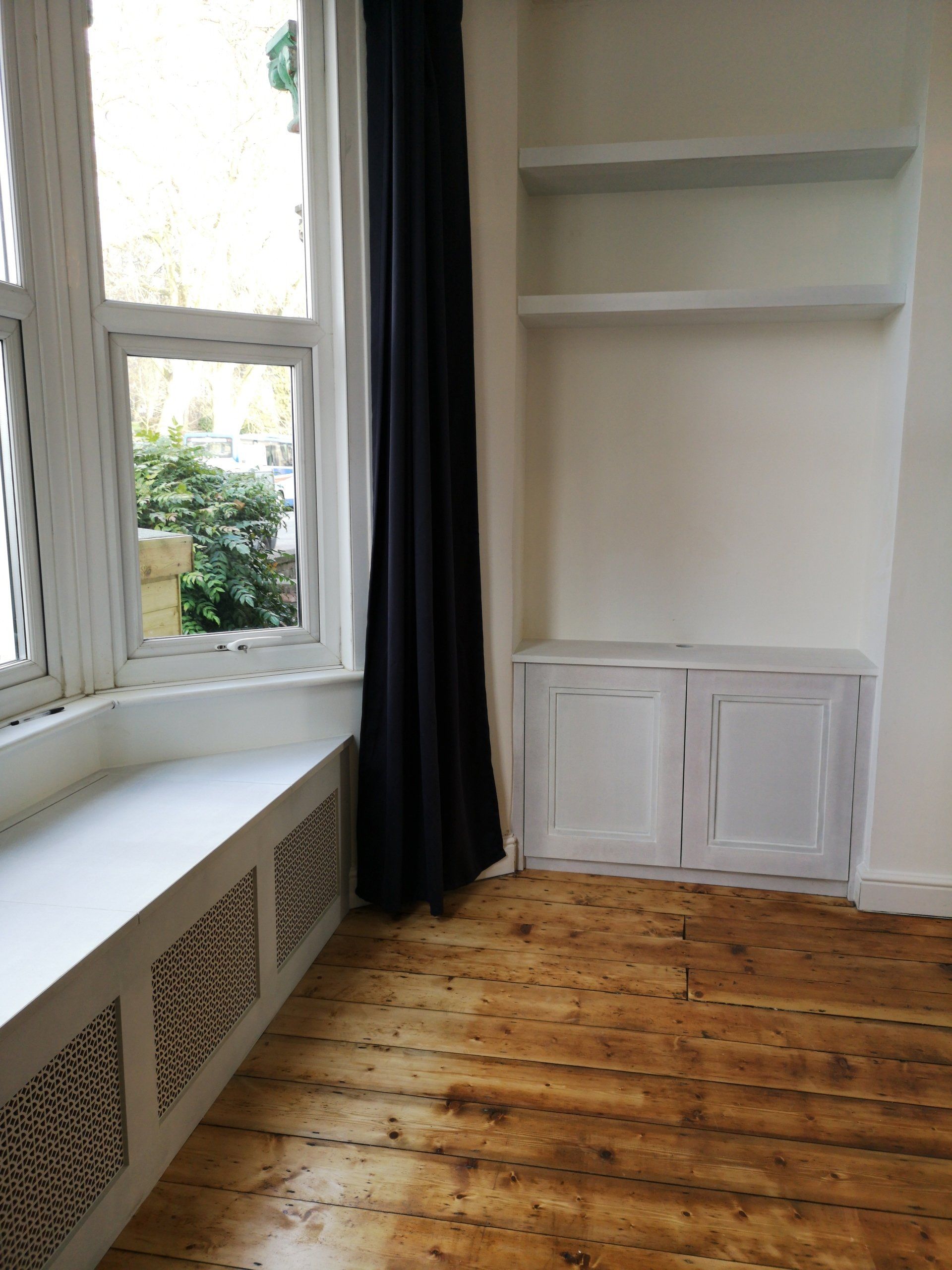 Fitted alcove unit in Bristol with floating shelves and window seat with decorative grille panels and lift up lid.