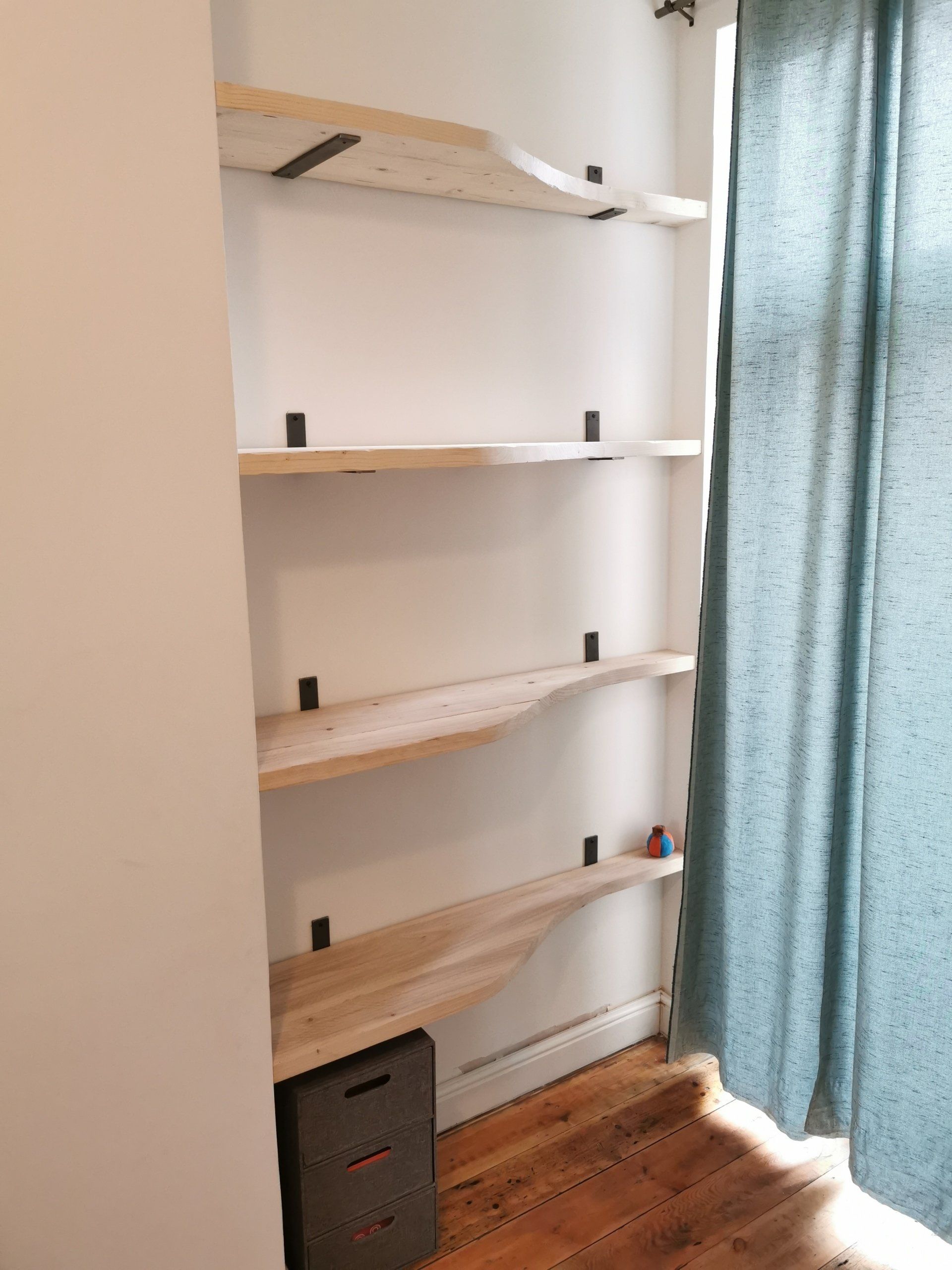 Scaffold board shelves with wavy edge fitted on raw steel brackets.