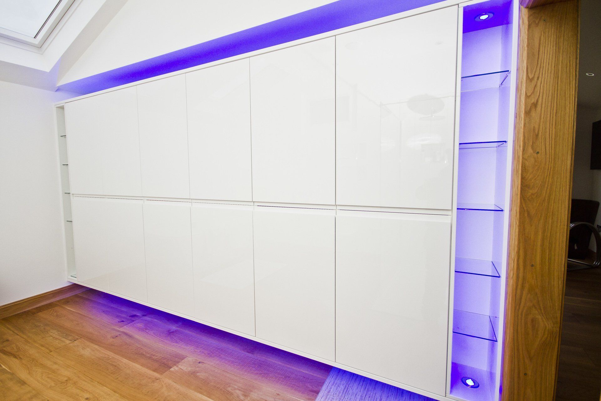Large wall of gloss white wardrobes with glass shelves and blue LED lights all round