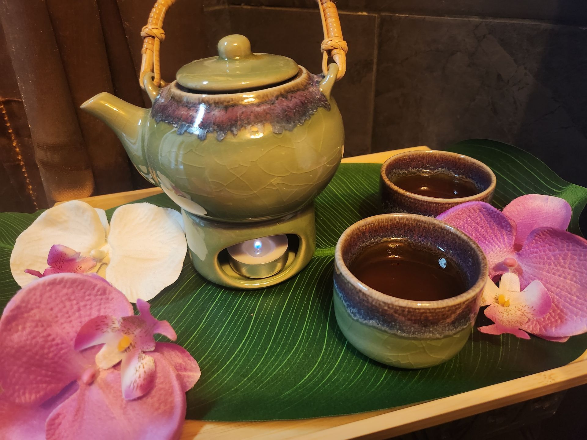 A tea set with two cups, a teapot, and orchids on a green leaf tray, ready for serving.