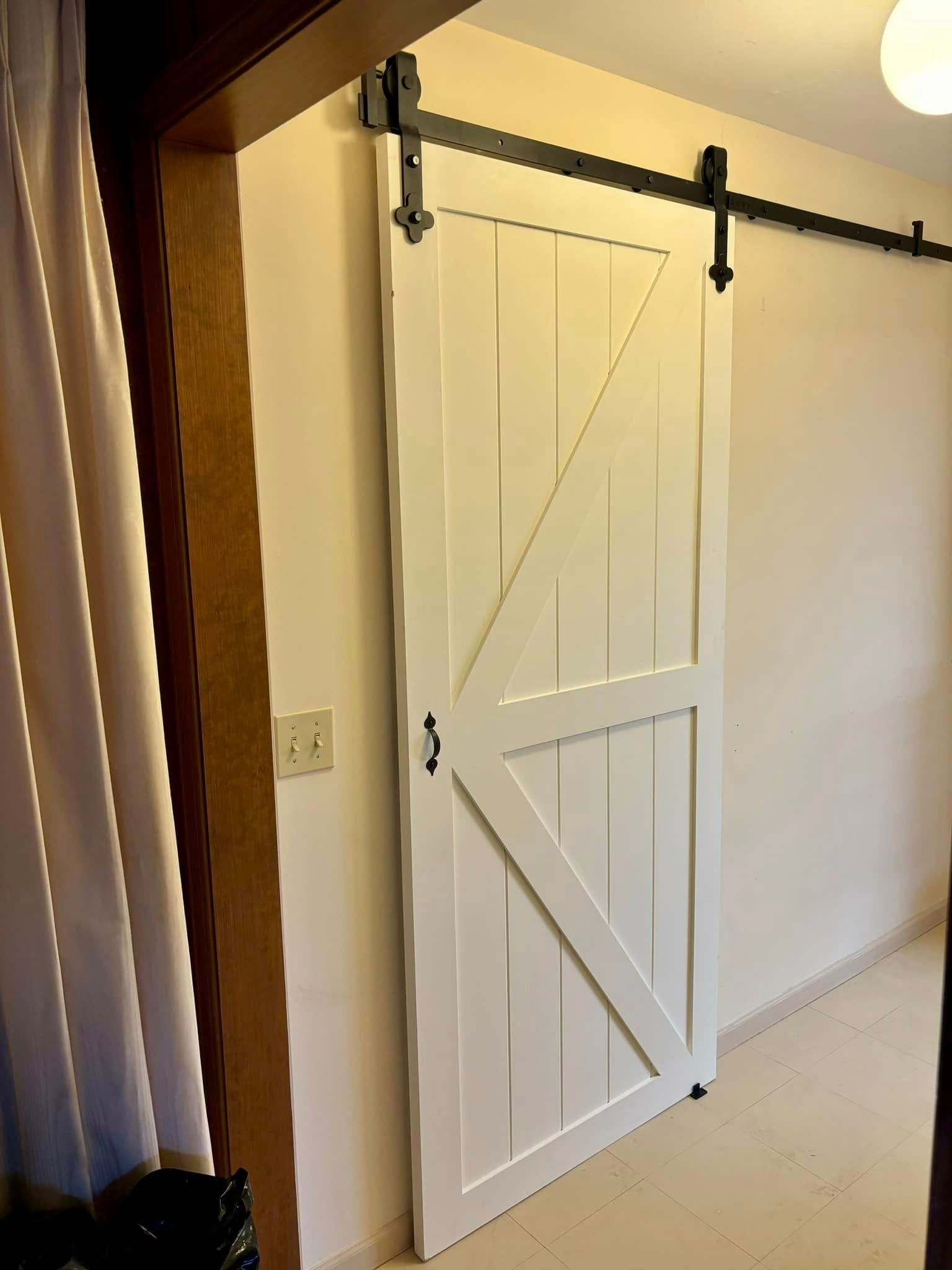 A white sliding barn door is hanging on a white wall in a room.