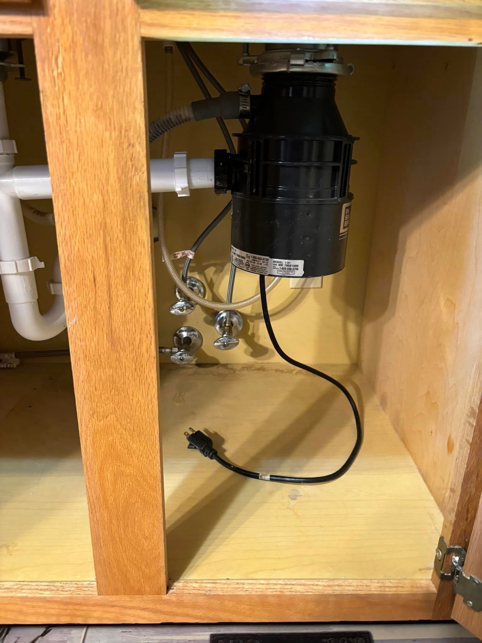 A garbage disposal is sitting under a sink in a kitchen cabinet.