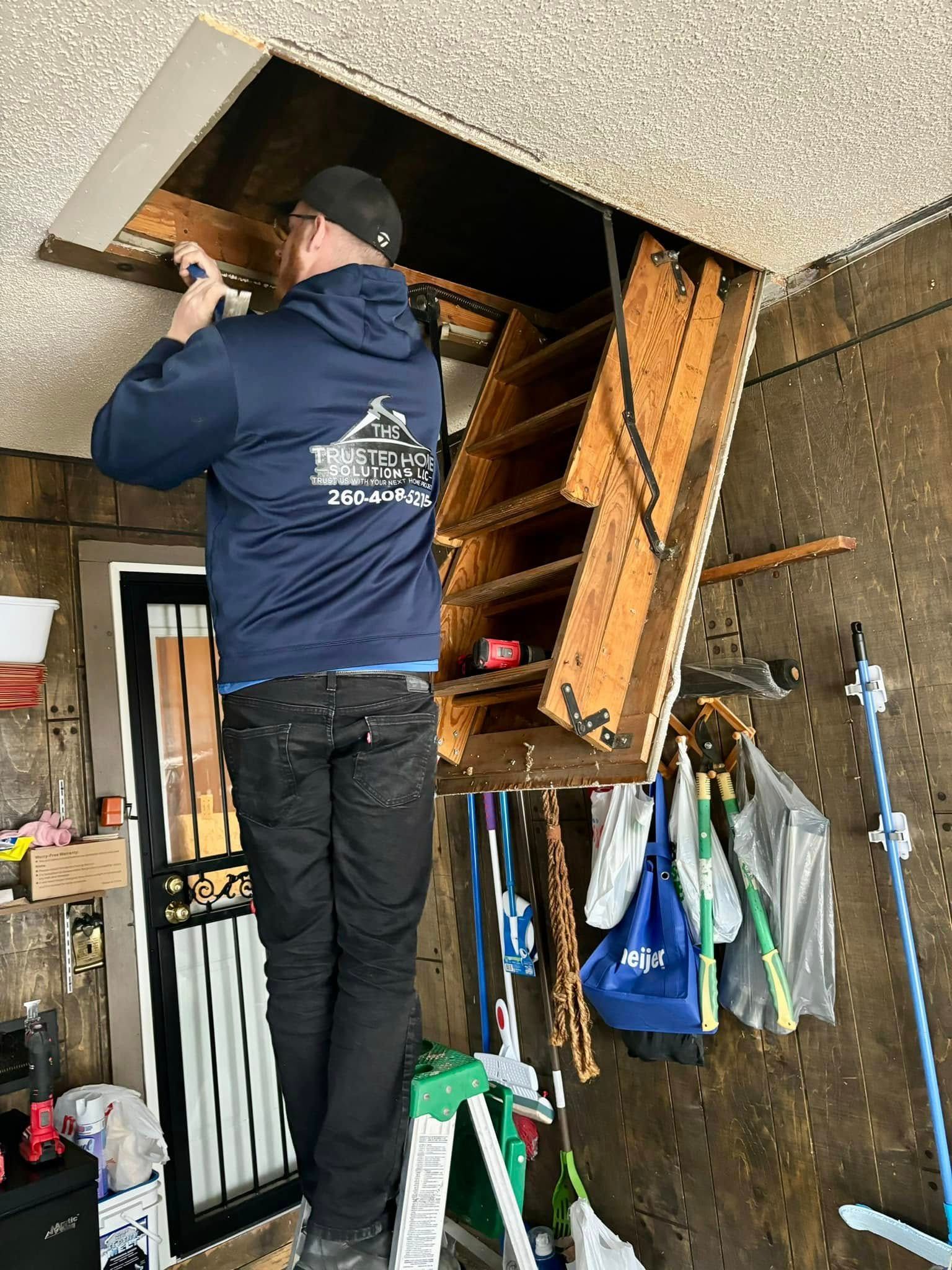 A man is standing on a ladder in an attic.