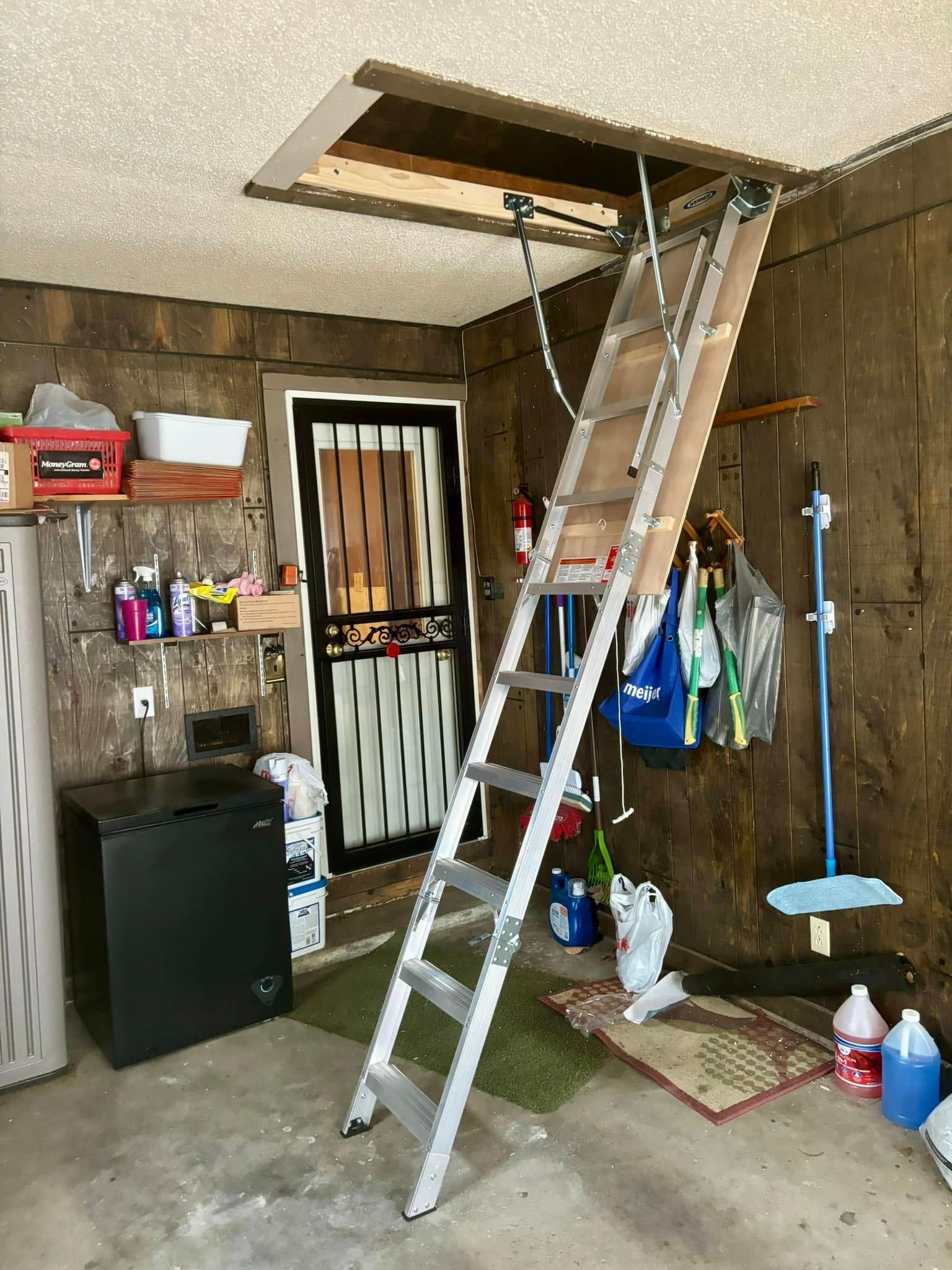 A ladder is going up to the attic in a garage.