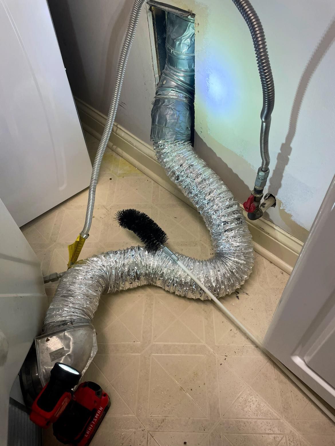 A hose with a brush attached to it is coming out of a hole in the wall.