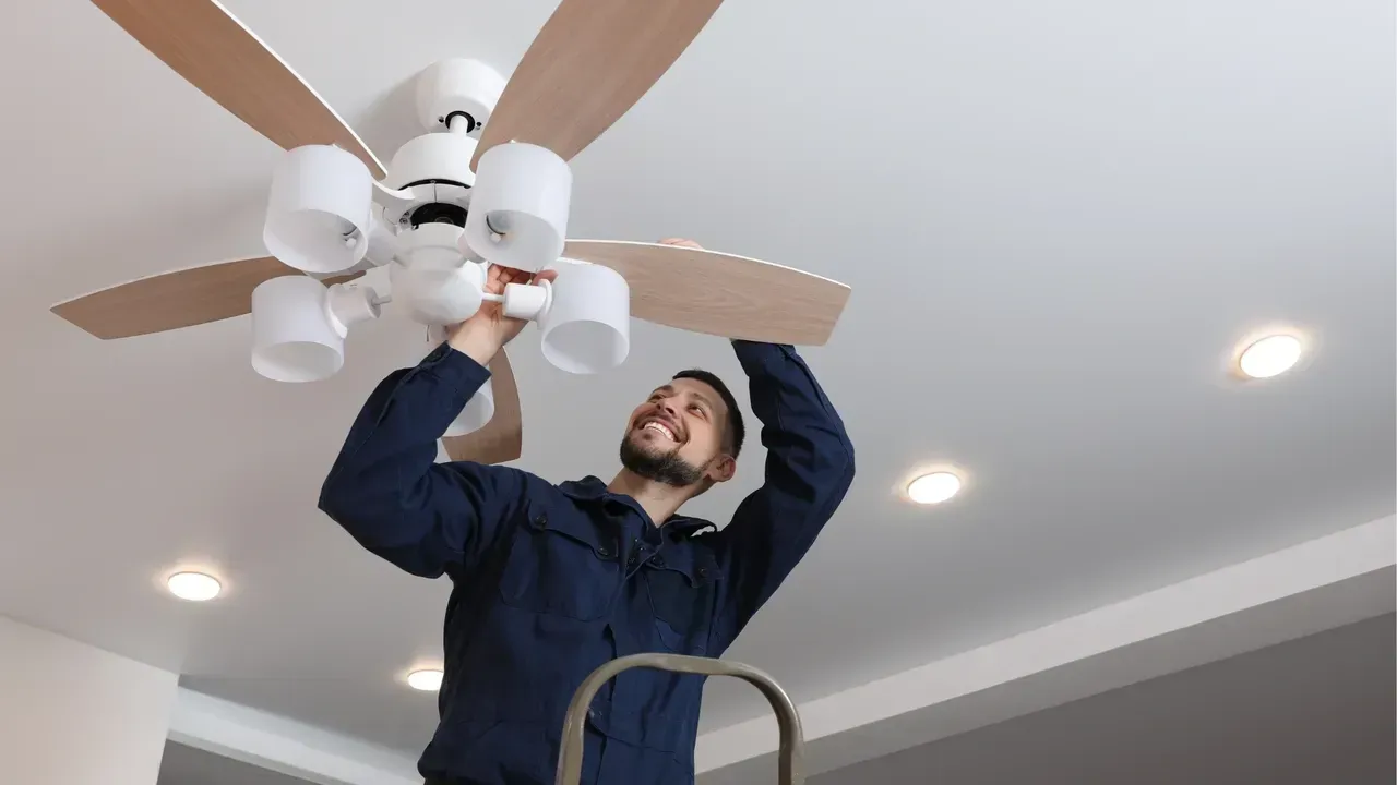 A man is installing a ceiling fan in a living room.