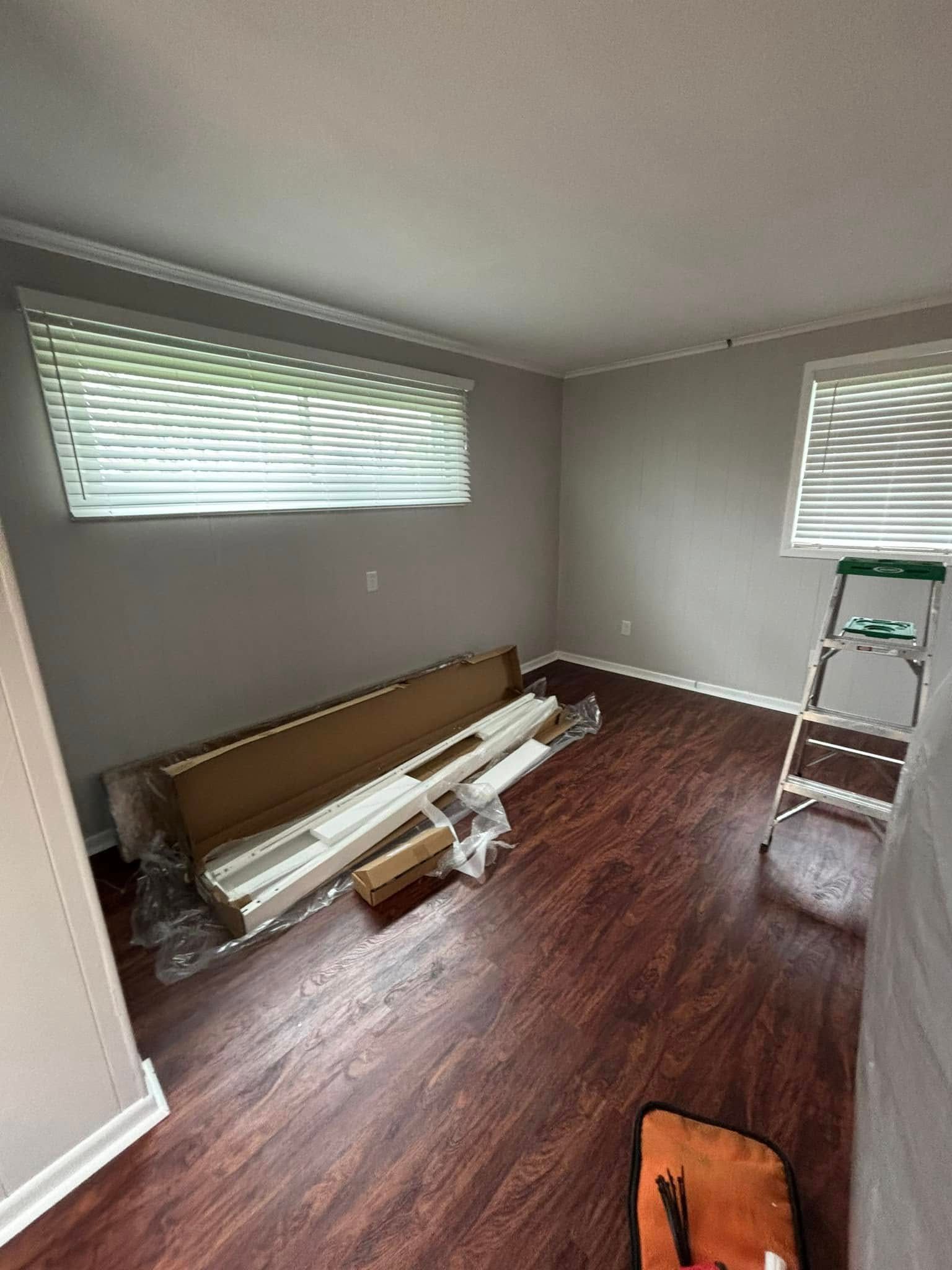 A living room with hardwood floors , blinds , a ladder and a window.