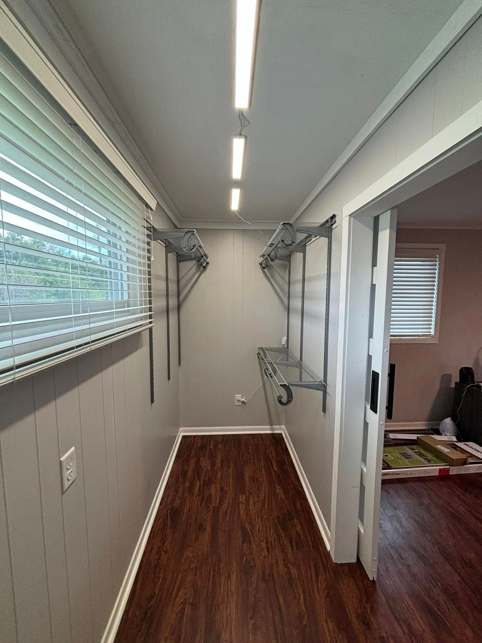 A walk in closet with wooden floors and a window.