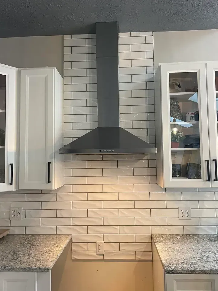 A kitchen with white cabinets , granite counter tops , and a stove hood.