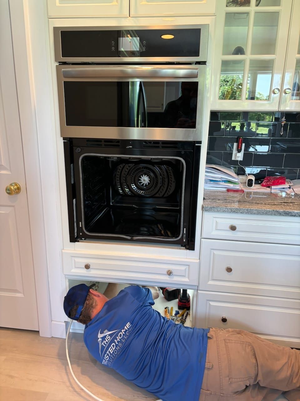A man in a blue shirt is working on an oven in a kitchen.
