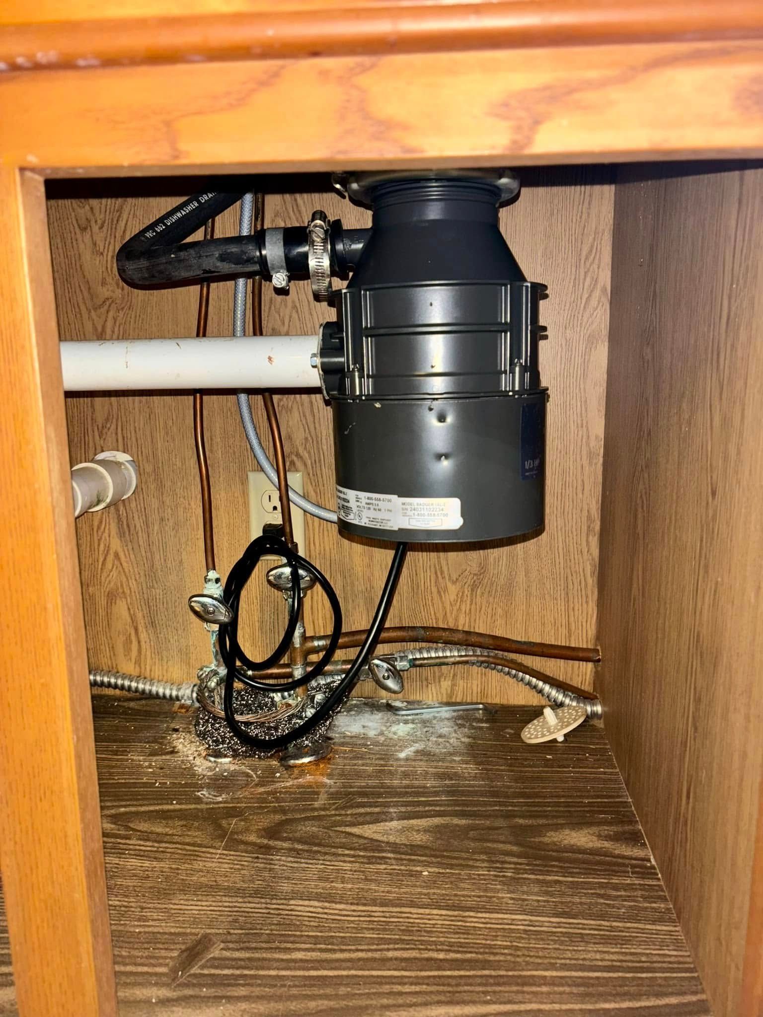 A garbage disposal is sitting inside of a wooden cabinet.