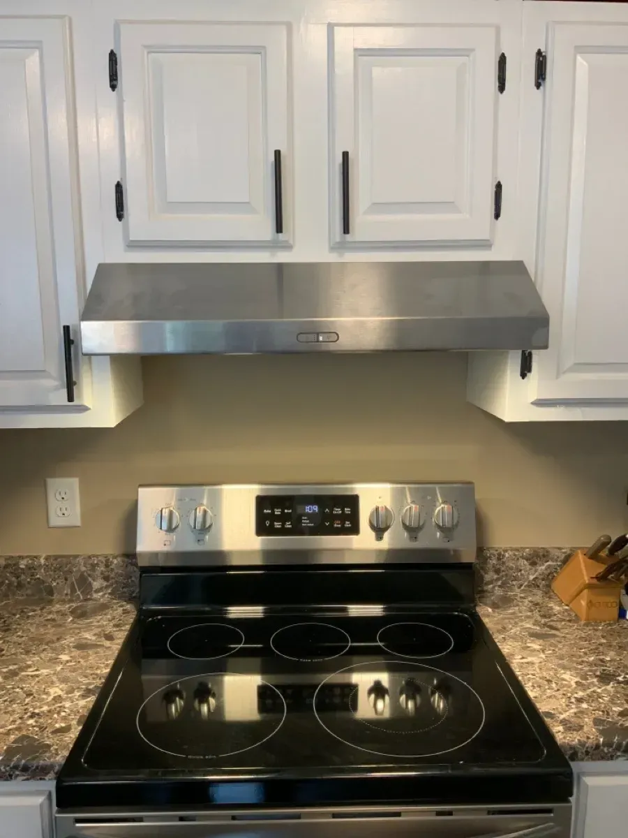 A stainless steel stove top oven with a hood above it in a kitchen.