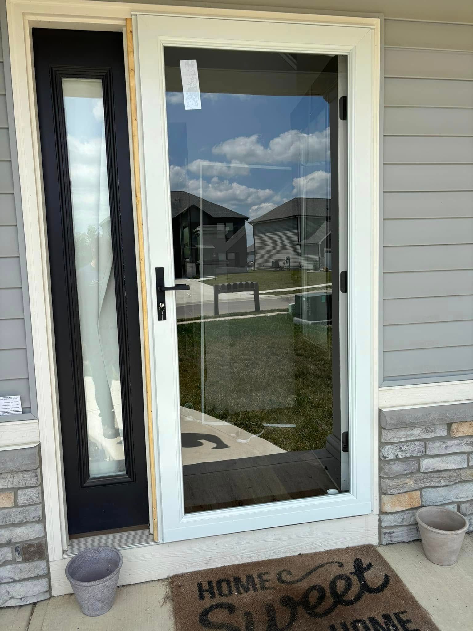 A black door with a white frame and a door mat on the porch of a house.