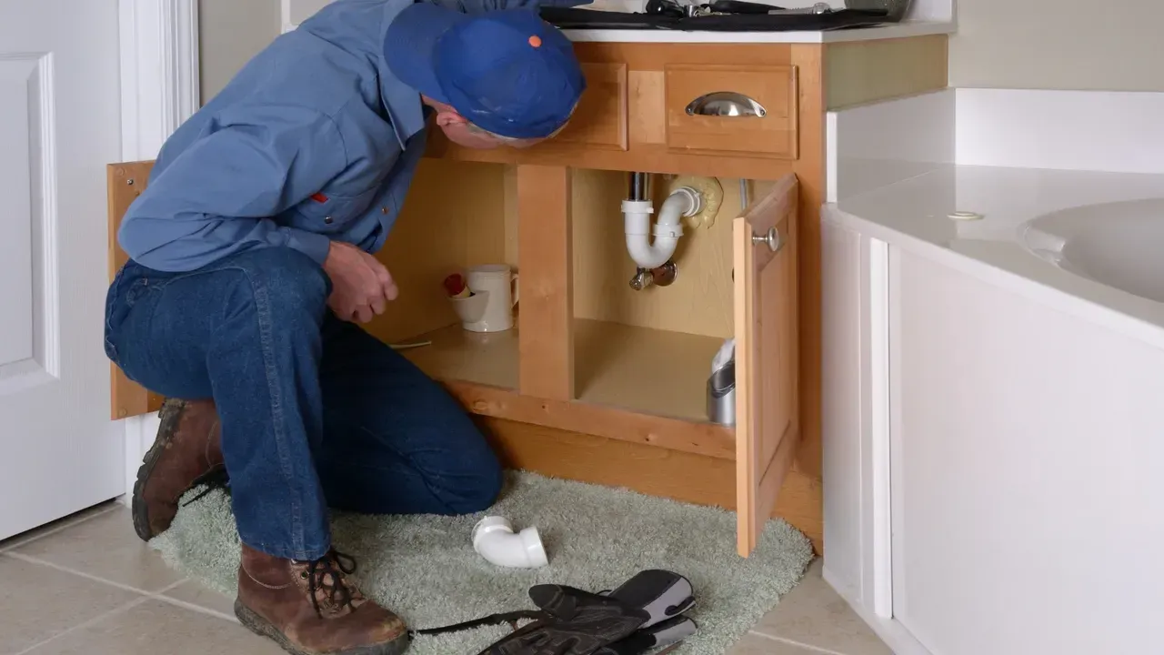 A man is kneeling down under a sink in a bathroom.