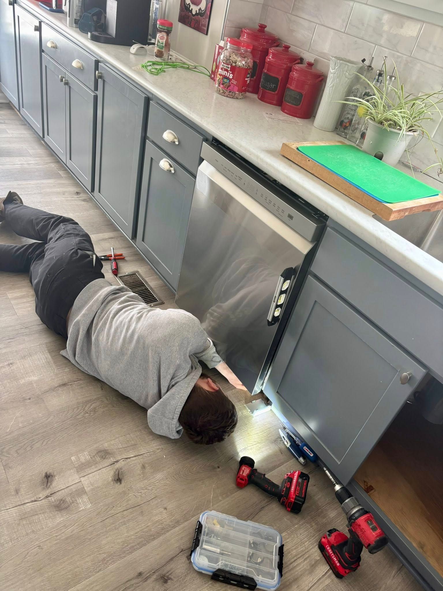 A person is laying on the floor in a kitchen working on a dishwasher.