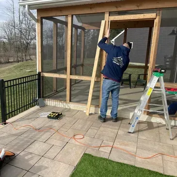 A man is working on a screened in porch with a ladder.