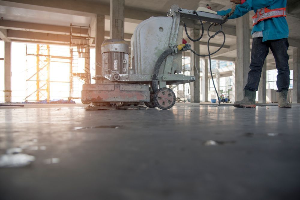 A Construction Worker Is Grinding A Concrete Floor With A Machine — Tuscany Concreting In Airlie Beach, QLD