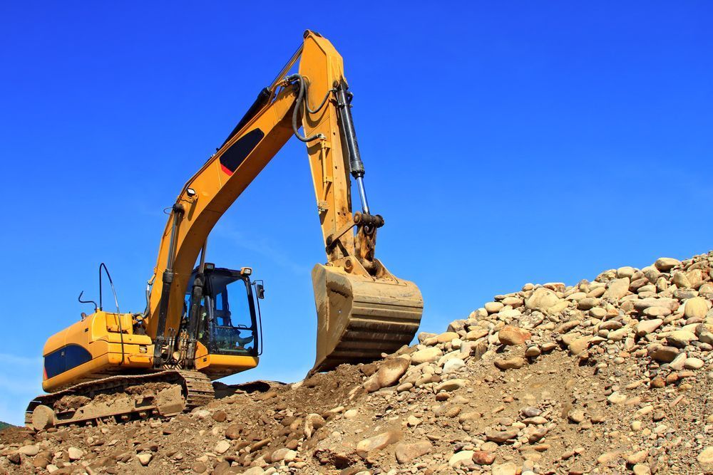 A Yellow Excavator Is Working On A Pile Of Rocks — Tuscany Concreting In Airlie Beach, QLD
