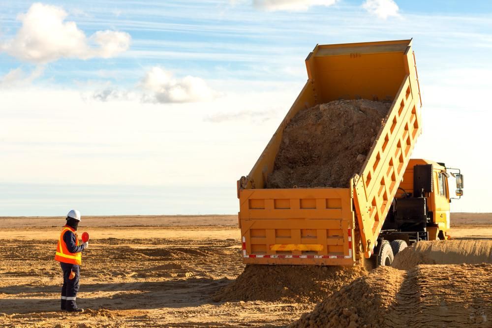 Yellow Tipper Truck Unloading Dirt On A Dirt Field — Tuscany Concreting In Cannonvale, QLD