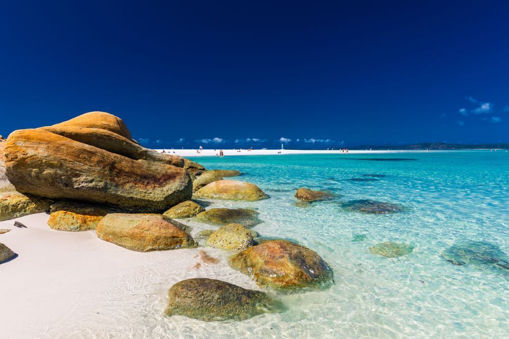 A Large Rock Is Sitting On Top Of A Sandy Beach Next To A Body Of Water — Tuscany Concreting In Whitsundays, QLD