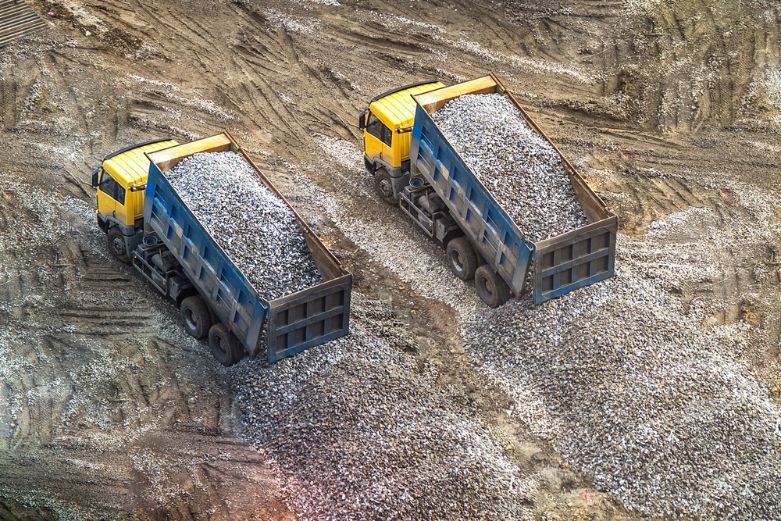 Two Dump Trucks Are Driving Down A Dirt Road — Tuscany Concreting In Airlie Beach, QLD