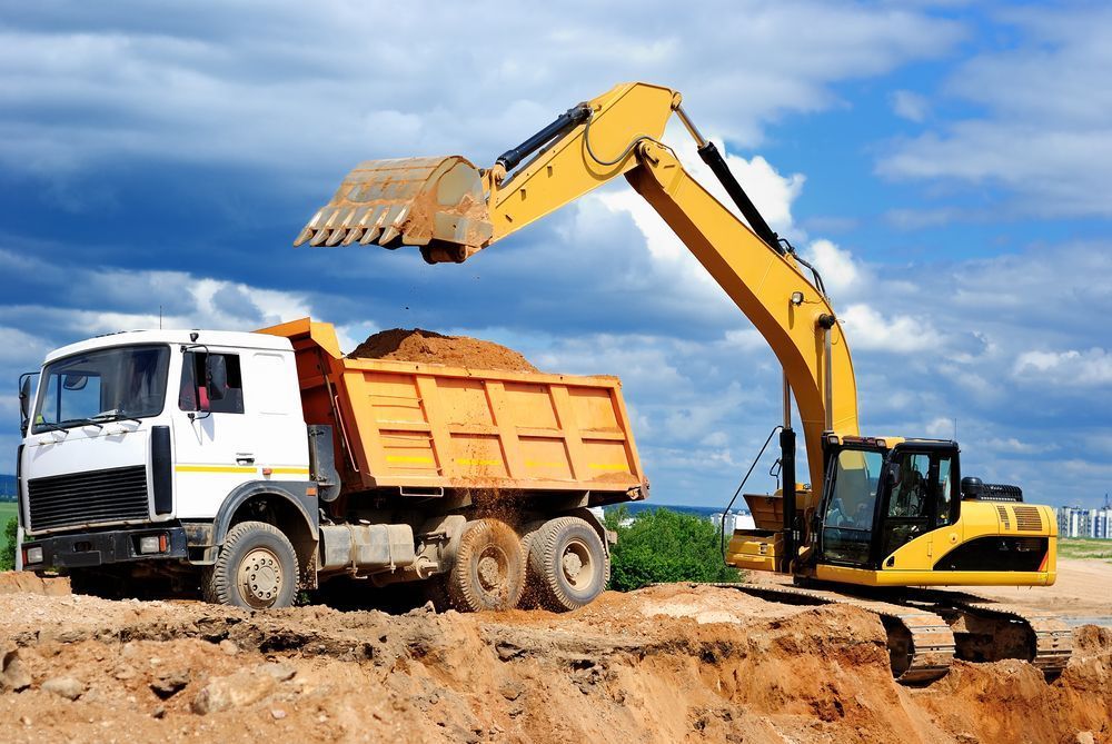 A Yellow Excavator Is Loading Dirt Into A Dump Truck — Tuscany Concreting In Airlie Beach, QLD