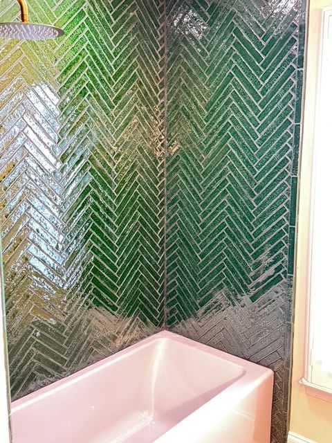 Green herringbone tile shower surround with a pink bathtub.