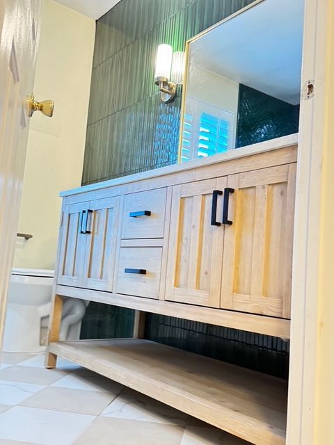 Bathroom vanity with light wood cabinets, dark hardware, and green tiled wall.