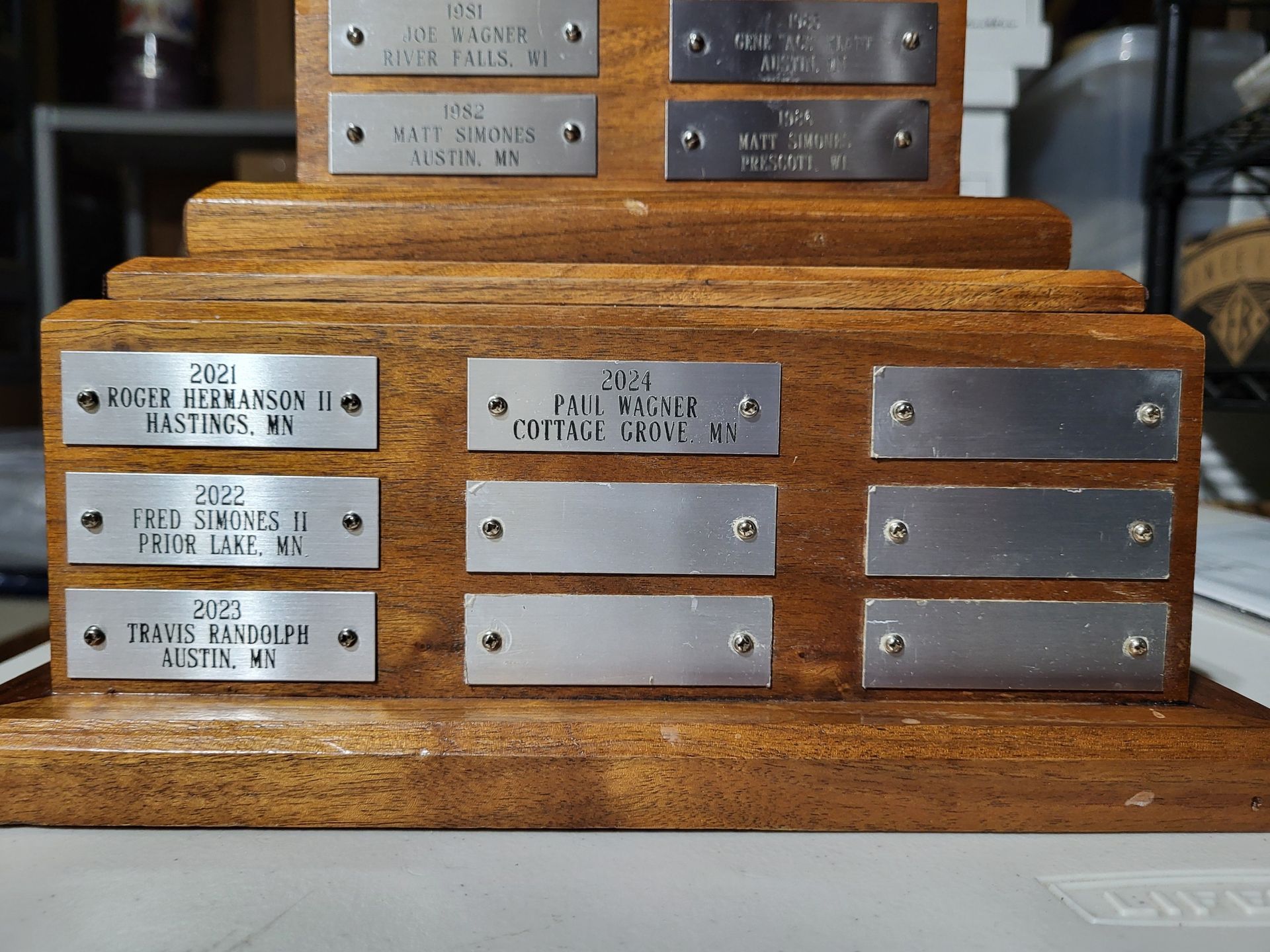 A wooden trophy base featuring engraved metal plates with years and names, including recent winners from 2021-2023.