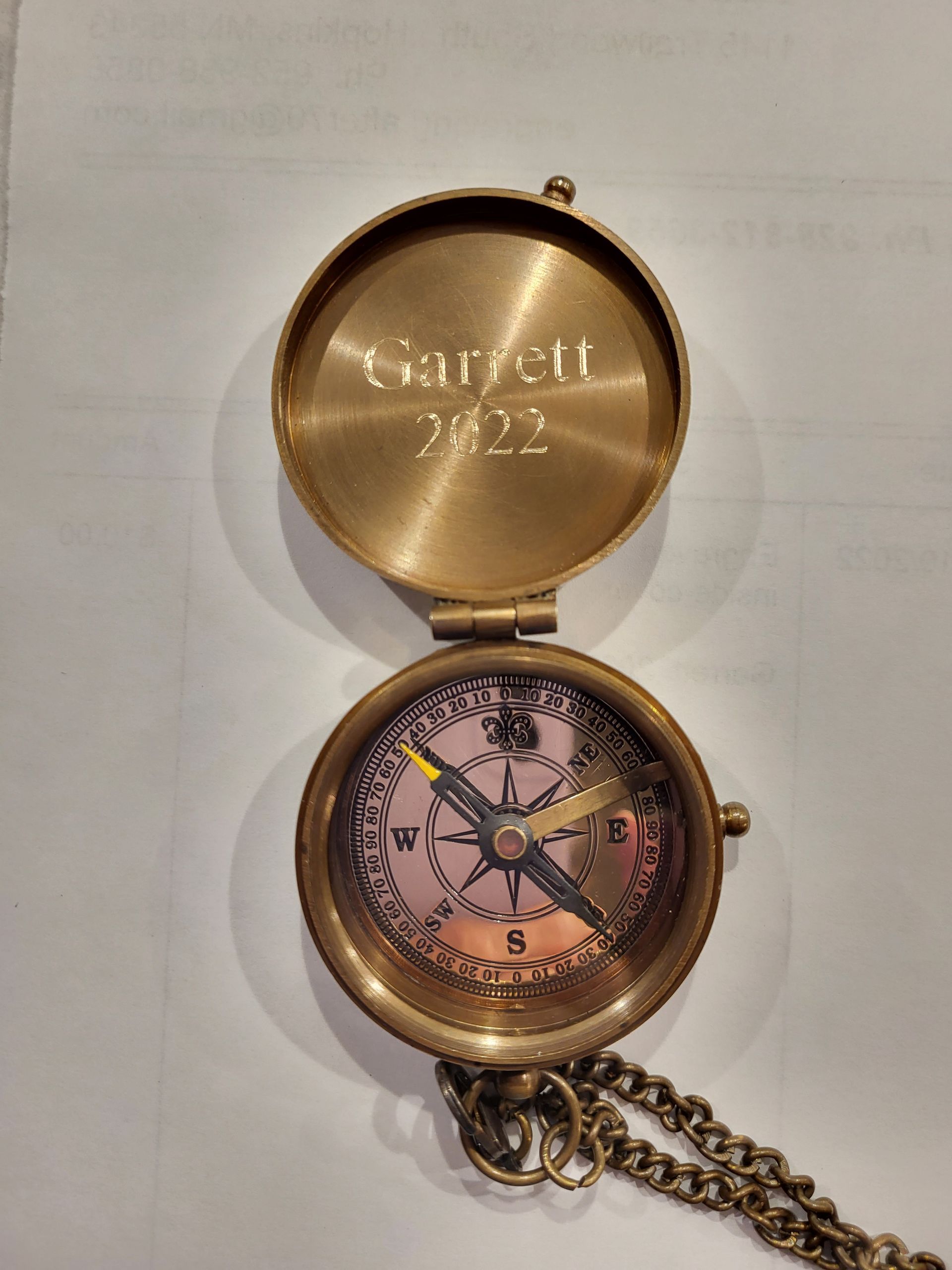 An open, brass-colored pocket compass with the name 