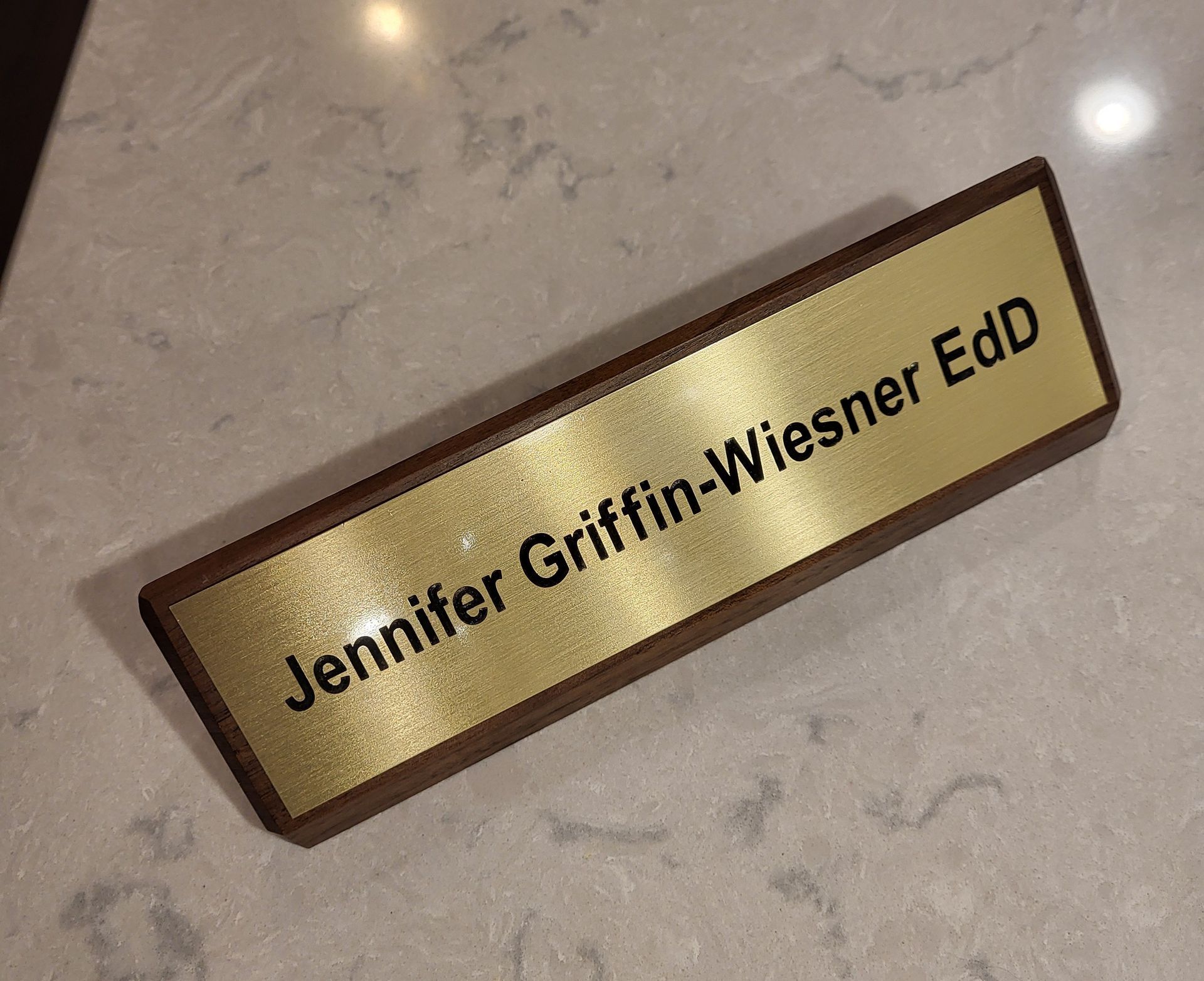 A gold-toned desk nameplate with brown trim featuring the black text 