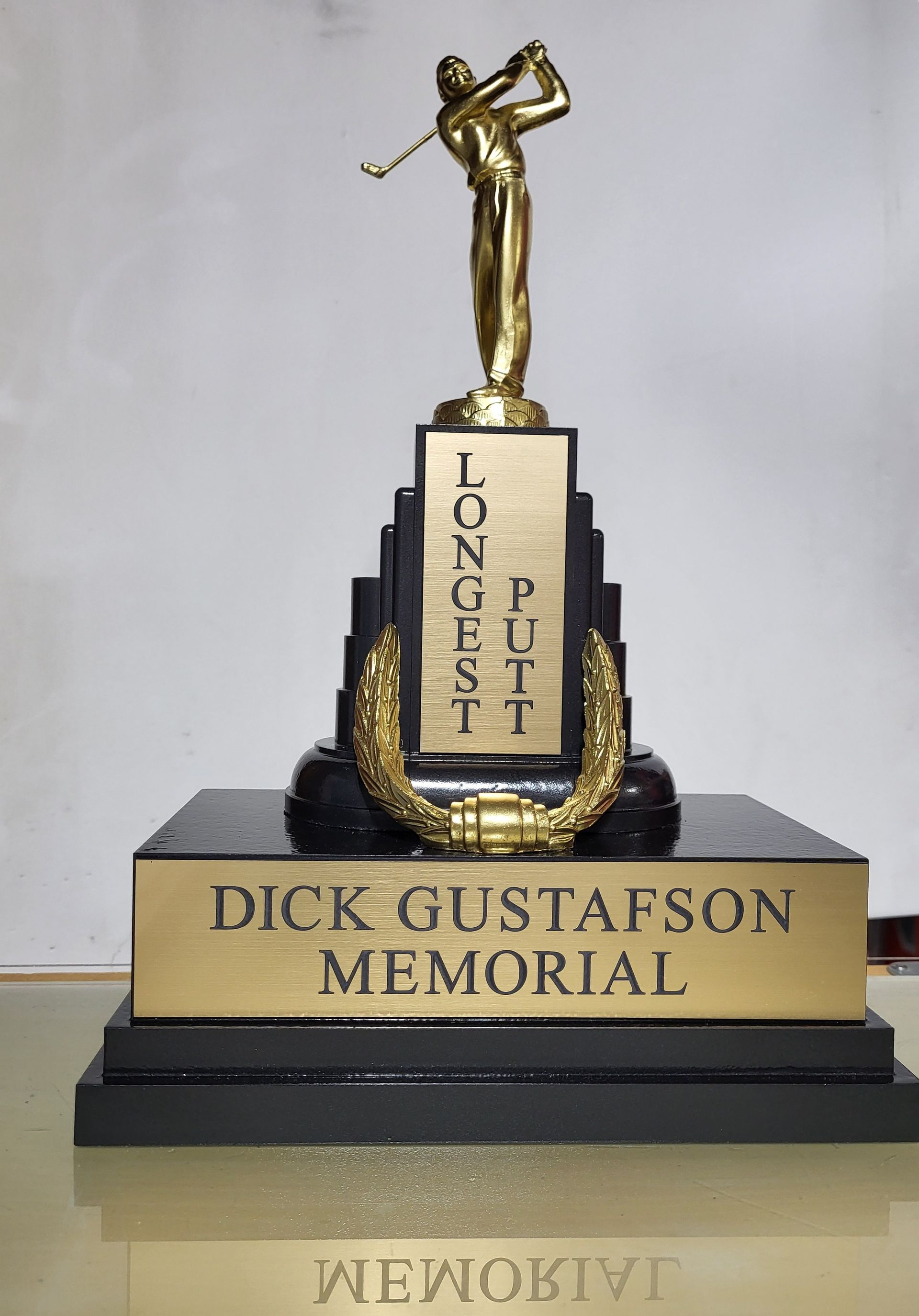 A trophy with a gold golf figure atop a tiered black base engraved with 