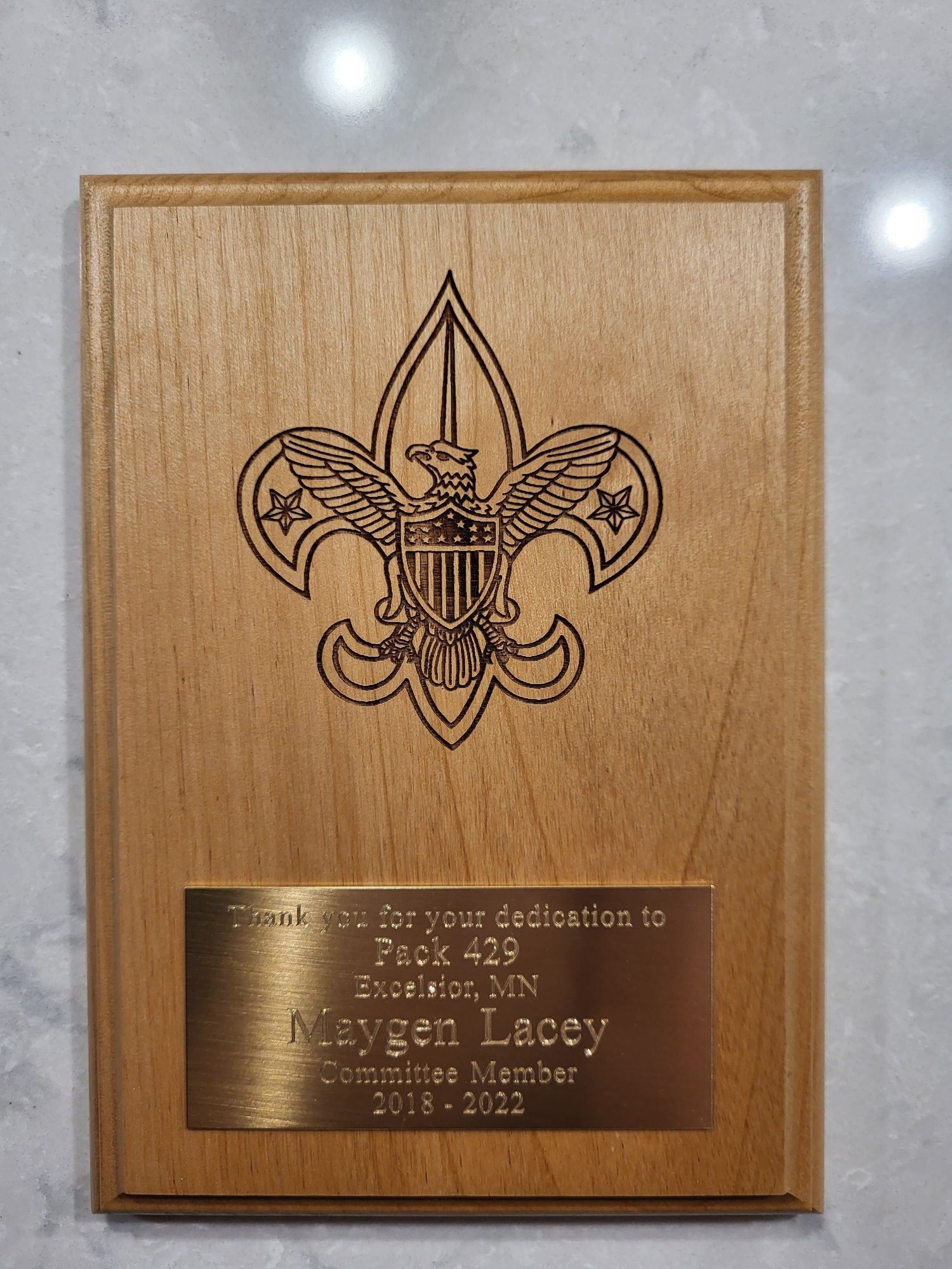 A wooden plaque with the Boy Scouts fleur-de-lis logo and a brass plate honoring Maygen Lacey, Pack 429, 2018-2022.