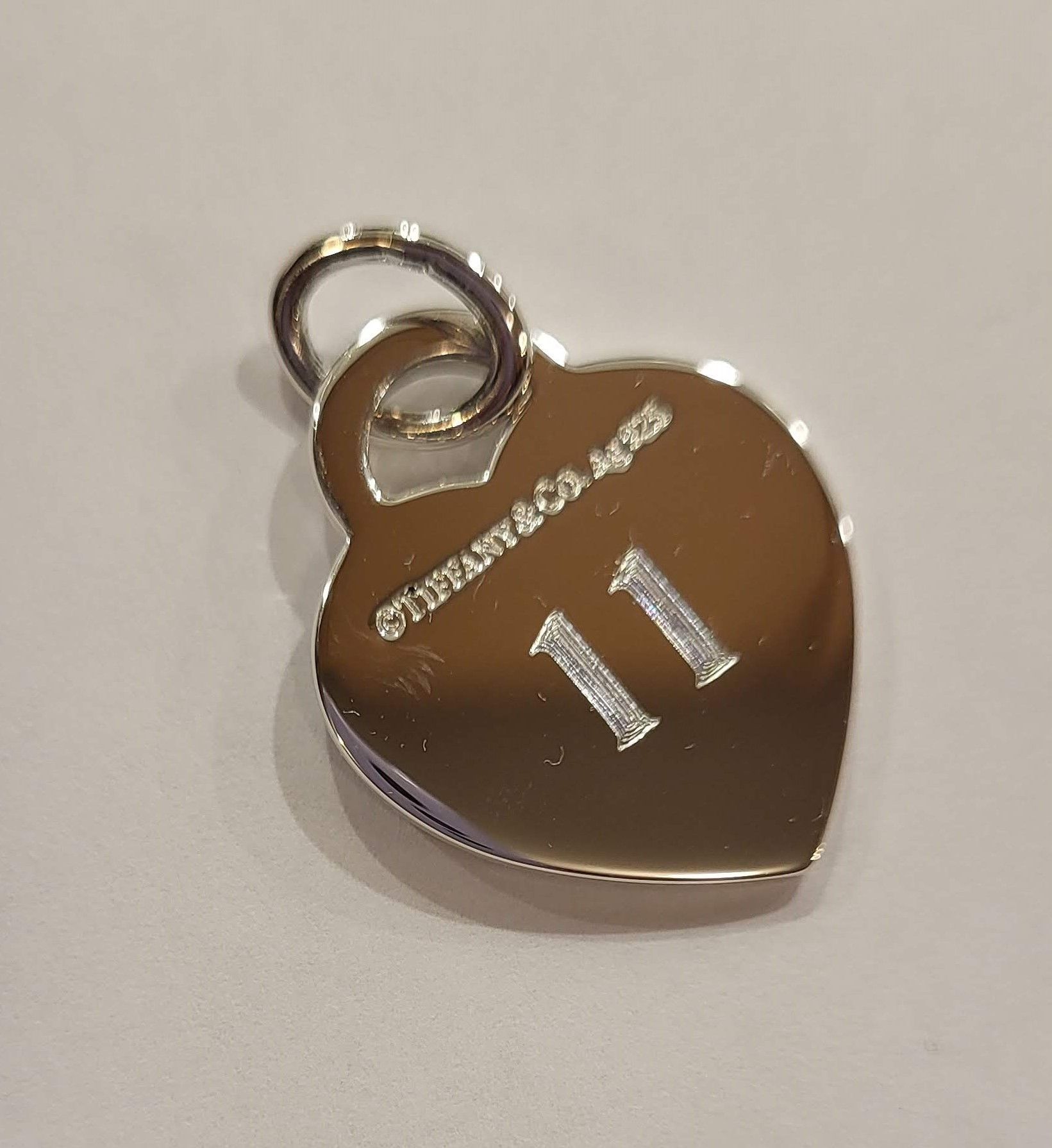 A silver-colored Tiffany & Co. heart-shaped charm with the Roman numeral 