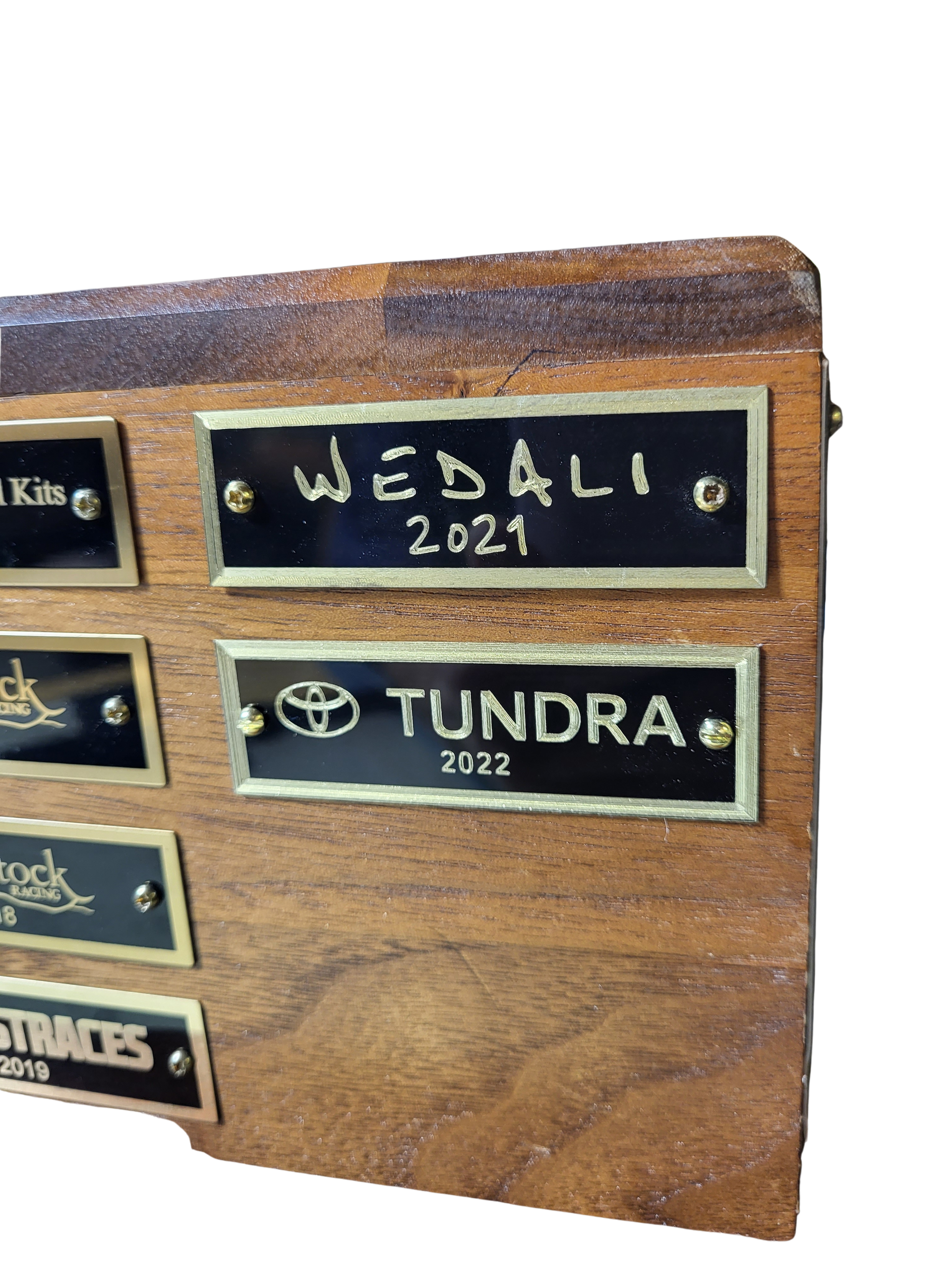 A wood plaque with several black nameplates, featuring engraved text including 