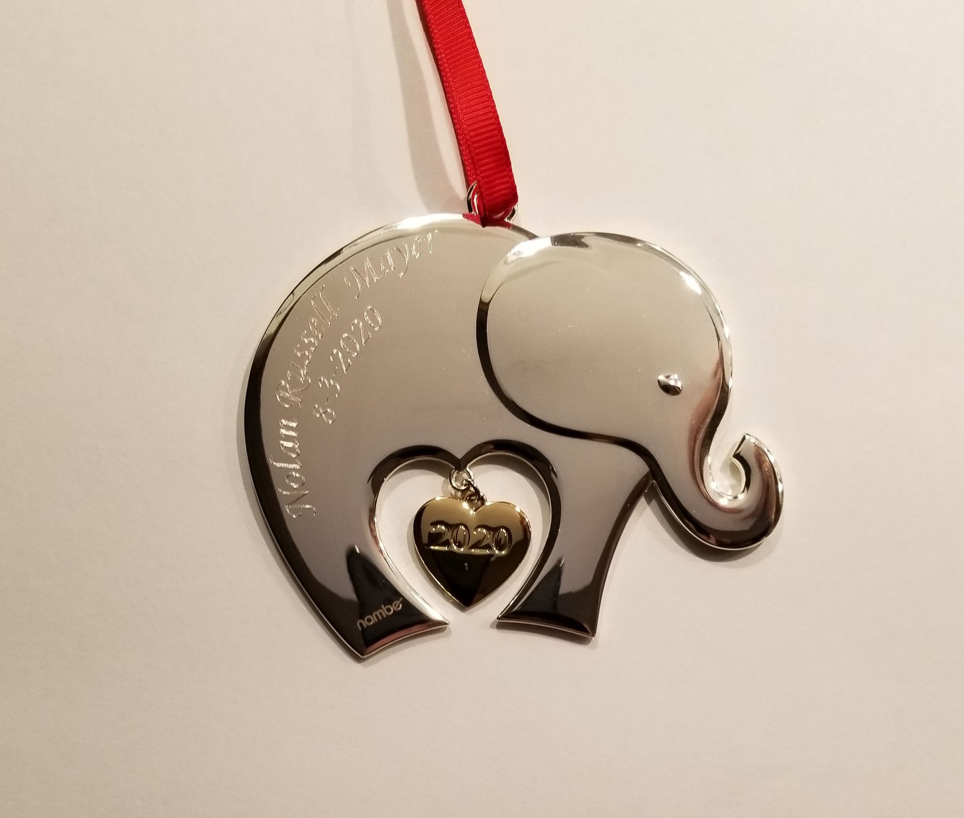 A silver elephant-shaped Christmas ornament with a hanging gold heart charm engraved with 