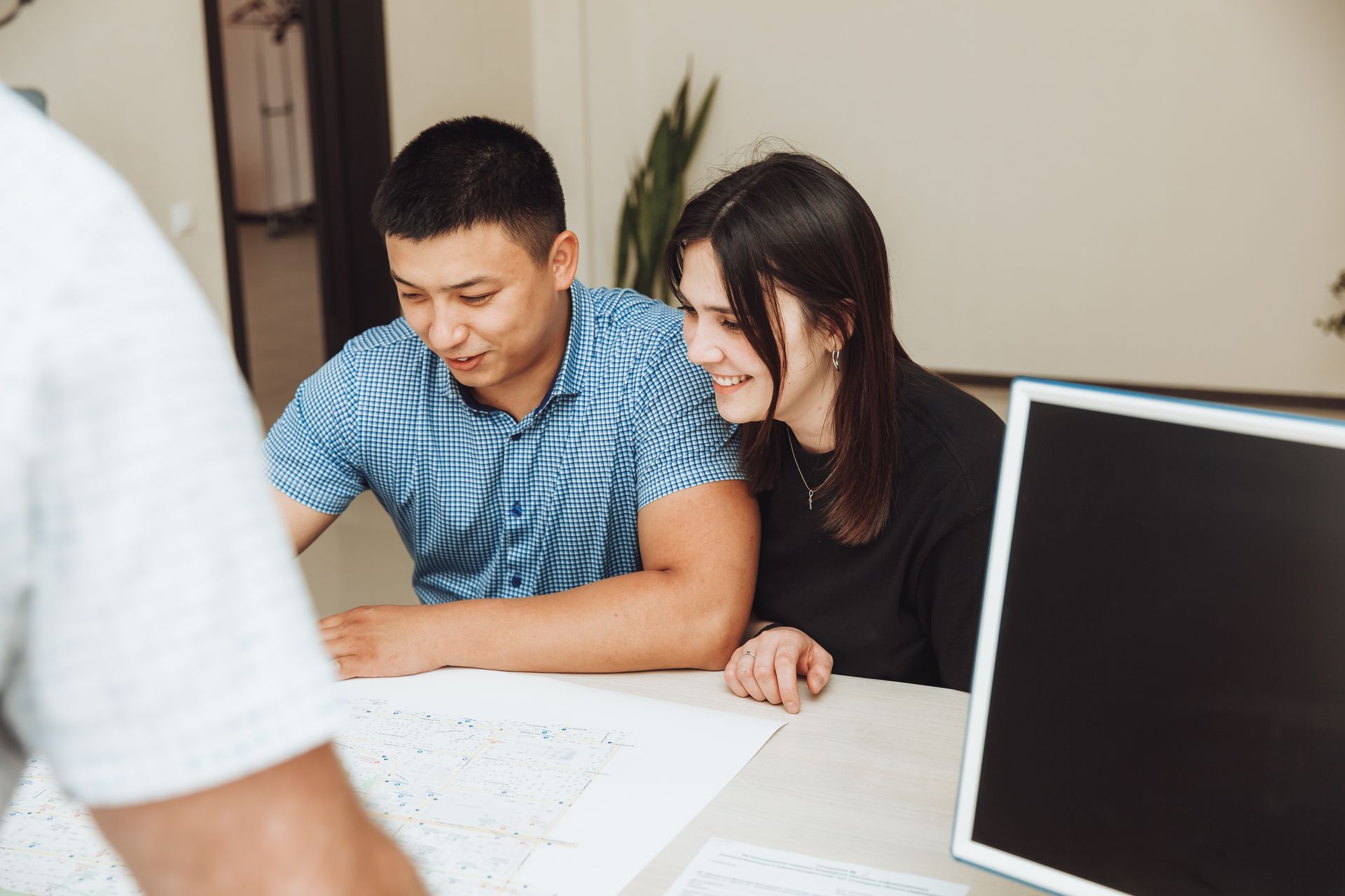 A man and a woman are sitting at a table looking at a computer screen.
