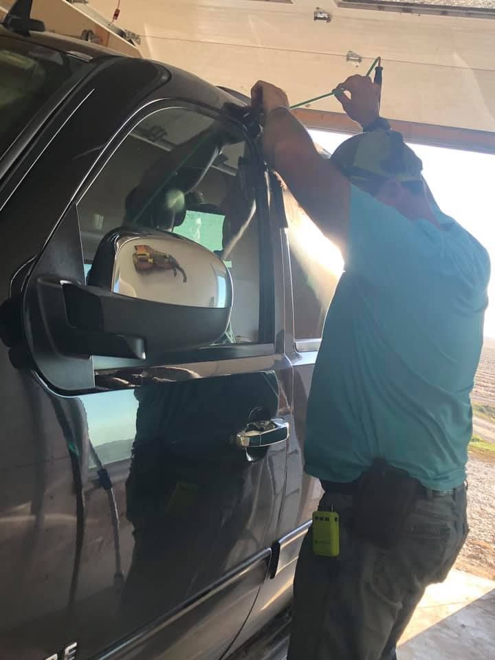 Person attaching something to a car's roof rack. Sunlit garage. Black truck.