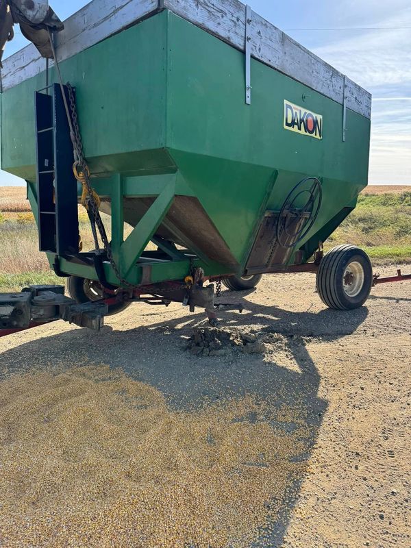 Green grain cart on gravel, outdoors, under a clear sky.