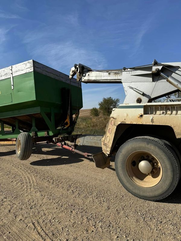 Green farm wagon being filled by a white truck with a lift against a blue sky.