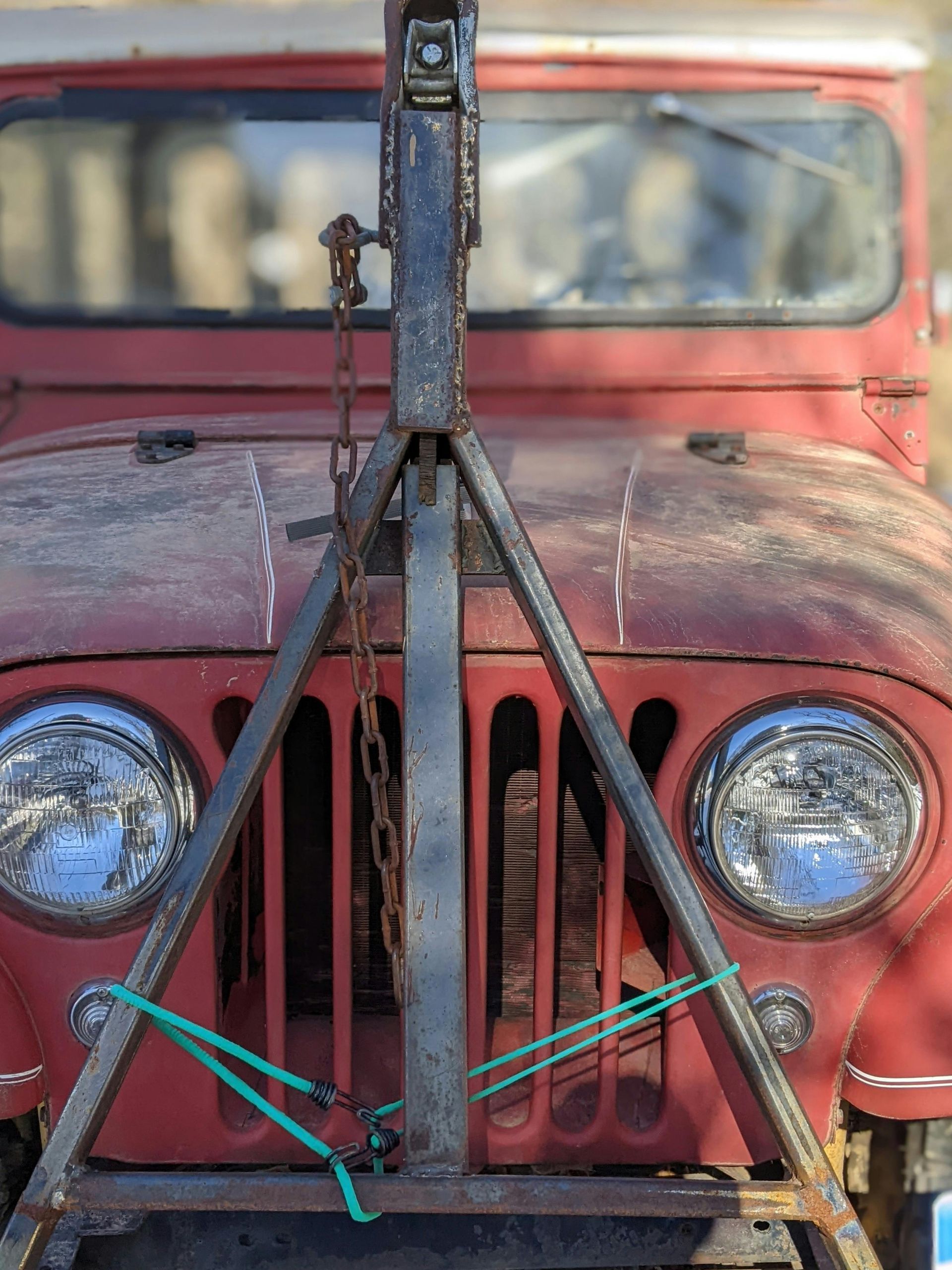 Red vintage Jeep with a homemade metal tow apparatus on the front.