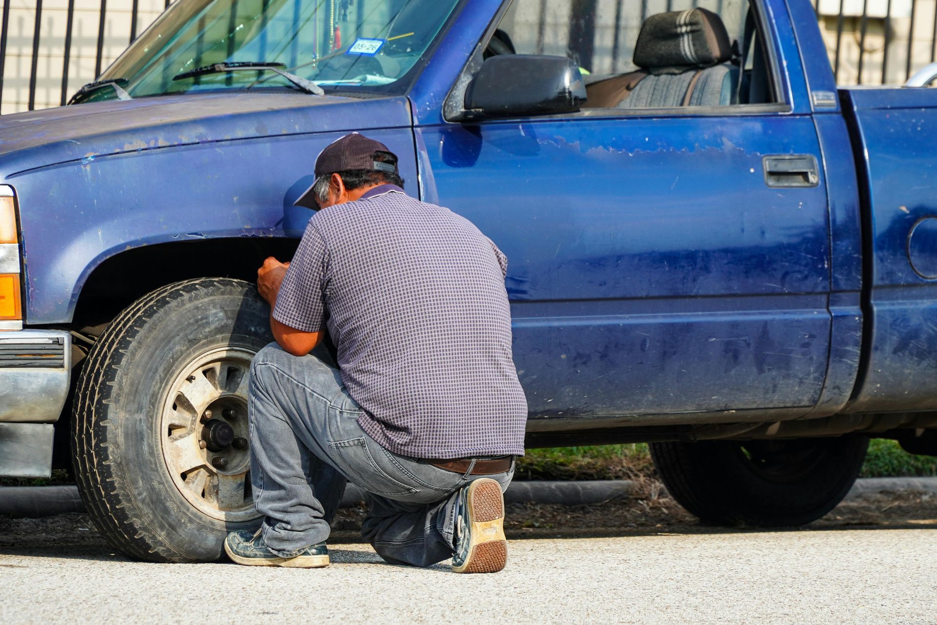 Person kneeling beside a blue pickup truck, appearing to work on the front tire.