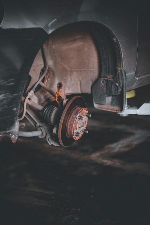Rusty car brake rotor and components, wheel removed, dark garage setting.