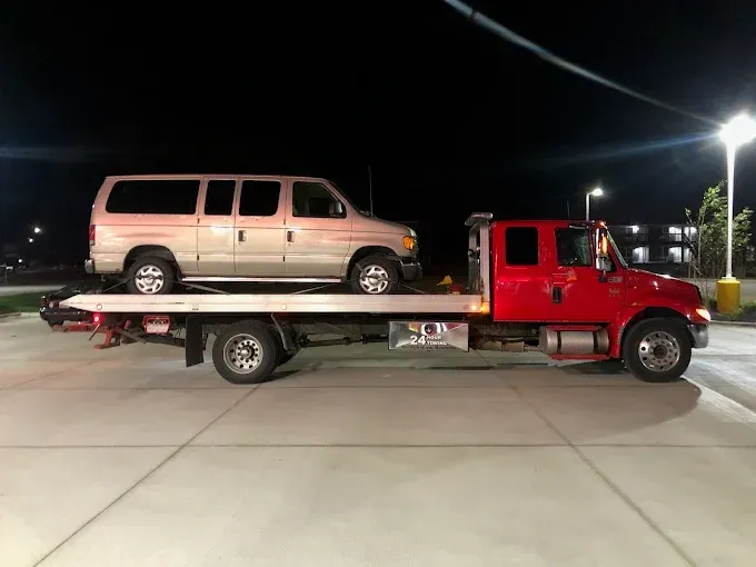 A tan van loaded on a red flatbed tow truck at night, under streetlight.