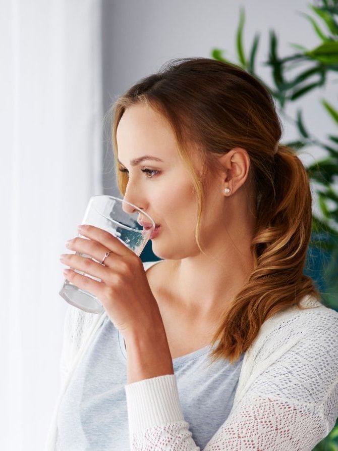 a woman is drinking a glass of water in front of a window